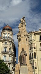 Valencia Monument and Architecture: A striking view captures a stately monument nestled amongst the elegant buildings of Valencia, Spain, framed by a dynamic sky. 