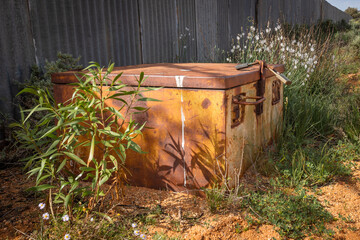 Naklejka premium A metal storage box from bygone days lies amongst the weeds next to a modern fence as an historical reminder of the past at Silverton, an ex-mining town near Broken Hill in New South Wales, Australia.
