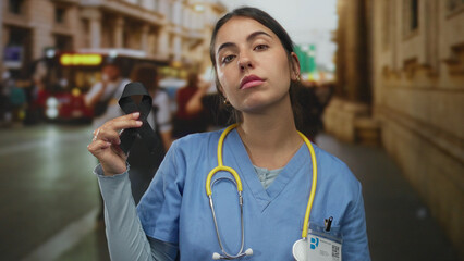 Young hispanic woman doctor with stethoscope holding black ribbon on busy street outdoors...