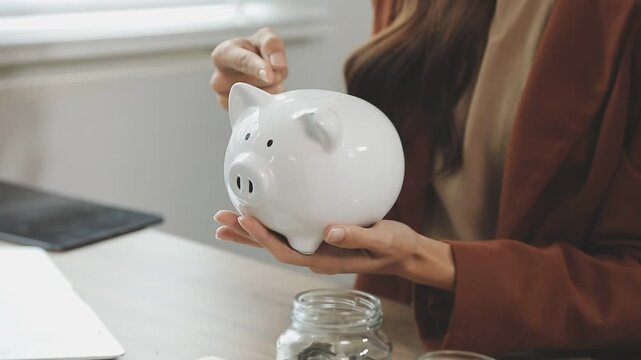 rAsian woman hand put coins in piggy bank,Saving money wealth and financial concept.