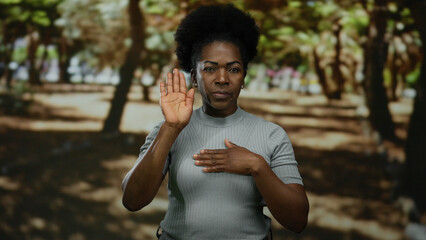 Fototapeta premium Woman gesturing oath in park with trees, demonstrating a serious expression, wearing casual attire outdoors.