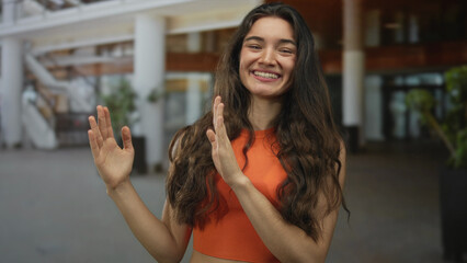 Hispanic teenager woman framing empty space with outstretched hands in a modern building; curiosity...