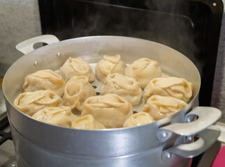 Delicious Manty, posture, khinkali is prepared in a special pot - mantoverde. Dishes of Asian, Buryat, Georgian cuisine. Aluminum steamer for cooking mantas on a stove in a home kitchen. Meat food.