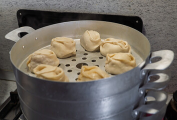 Delicious Manty, posture, khinkali is prepared in a special pot - mantoverde. Dishes of Asian, Buryat, Georgian cuisine. Aluminum steamer for cooking mantas on a stove in a home kitchen. Meat food.