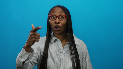Woman smiling in striped shirt with bright glasses and expressive gestures against an isolated blue wall shows confidence and joy.