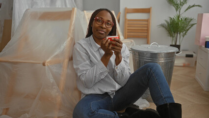 Woman relaxing in new home living room sitting on the floor with a cup surrounded by unpacked...