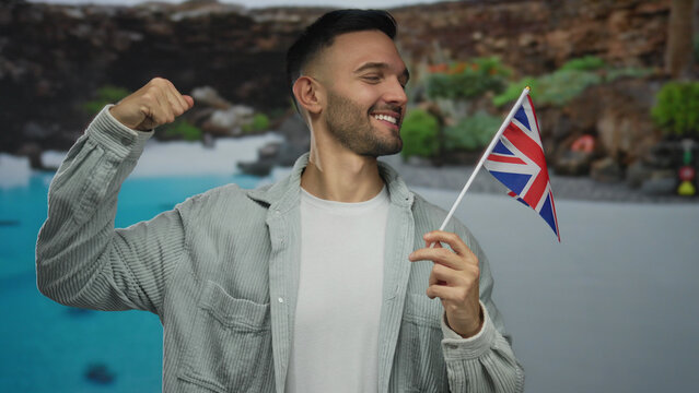 Hispanic man in a hotel swimming pool confidently flexing his arm while holding a uk flag, symbolizing joy and patriotism.