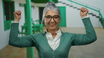 Senior woman with glasses and grey hair smiling and flexing arms in an outdoor street setting,...