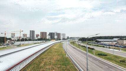 Modern cityscape with empty highway, residential high-rises, and construction cranes on the horizon under cloudy sky, symbolizing urban development, infrastructure growth, and real estate expansion