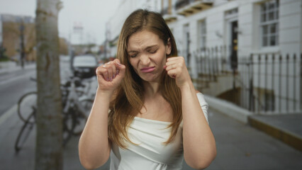 Young caucasian woman mimes crying tears with fingers on urban street sidewalk near bicycles and...