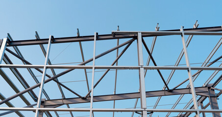 Steel beams form the skeletal steel frame structure of a building under construction, contrasting with a bright blue sky