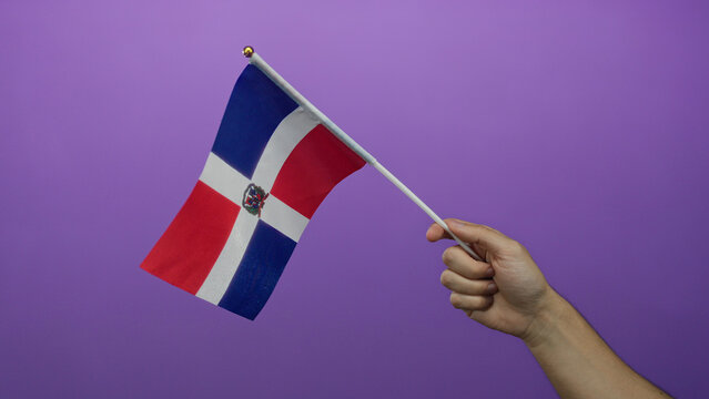 Man holding dominican republic flag against purple background with isolated hand showcasing national pride.