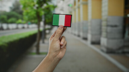 Hand holding italian flag embroidery on city street background, showcasing patriotism and cultural...