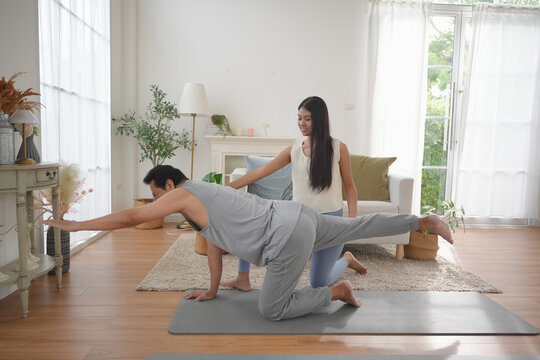 Asian mature man and young woman practicing yoga at home, smiling and supporting each other while stretching and balancing together. - Powered by Adobe