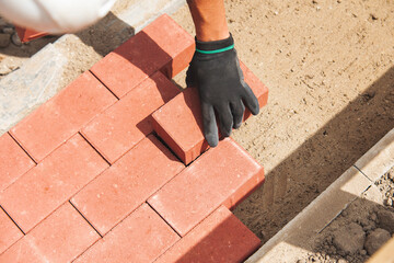 Close-up of Worker laying red paving bricks on newly constructed pathway