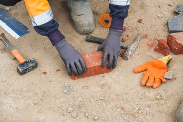 Close-up of builder breacking red paving bricks to right size to fit into path pattern