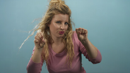 Woman making clawing hand gestures toward camera in a blue studio setting, wearing a pink long...