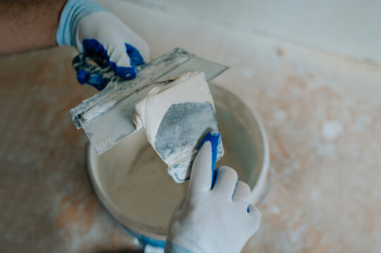 Person using putty and trowel for indoor plastering during repair