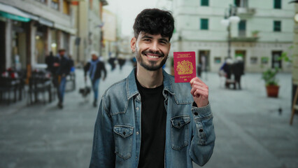 Man smiling holding uk passport in city street, wearing denim jacket with casual urban backdrop,...