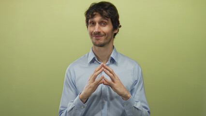 Man gesturing with hands against green studio wall, smiling with fingertips steepled and looking...