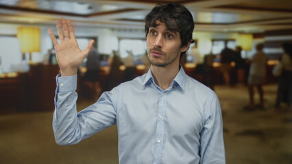 Man in blue shirt raises open palm for attention in hotel building; calm respect courtesy...