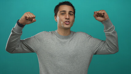 Young man exuding joy and confidence with clenched fists against vibrant teal background,...
