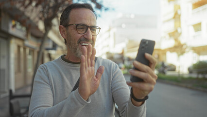 Man smiling at smartphone in urban street setting, wearing glasses, appearing happy and engaged, with a casual style, capturing a vibrant, lively city environment.