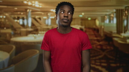 Young african american man wearing red t shirt holds wrist at restaurant bar counter; uncertainty reflection.