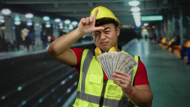 Man wearing construction vest holding us dollars at railway station making loser gesture showcases industrial and finance themes in public transport setting. - Powered by Adobe