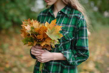 The girl is holding a bouquet of autumn maple leaves. 