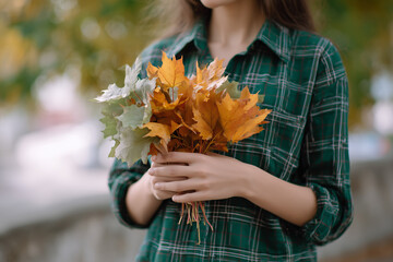 The girl is holding a bouquet of autumn maple leaves. 