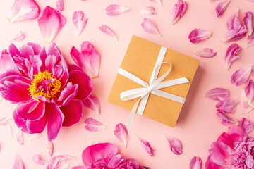 Gift box with white ribbon and pink peony flowers on pastel background with scattered petals
