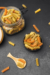 Colorful pasta in a jar and bowl on a dark background for culinary inspiration