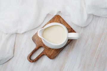 creamy milk in white pitcher on wood board with white cloth, top view