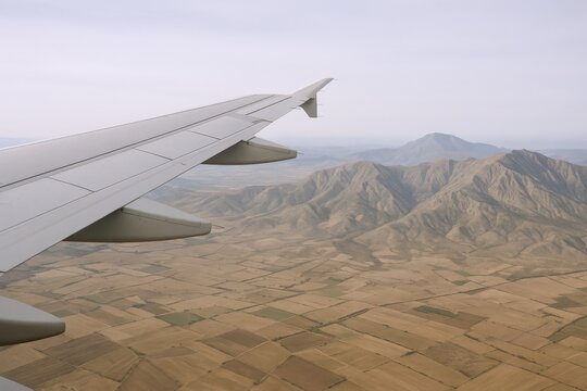 Aerial View of Brown Fields and Distant Mountains Through Airplane Window on a Cloudy Day