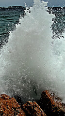 Dramatic wave crashes on coastal rocks. Powerful sea spray and foam erupt.