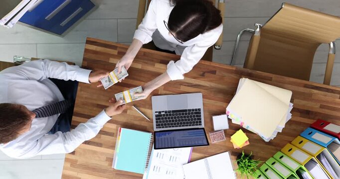 Man client offers neatly stacked bundles of dollar bills to woman director. Female verifies quantity and authenticity of money wad. Slow motion