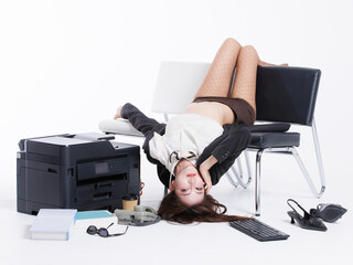 Asian pretty young woman confident long hair in office costume lying upside down on bench, poses playfully beside printer books sunglasses keyboard landline phone shoes in white studio fashion setting