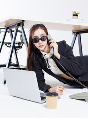 Asian pretty young cute woman confident in office costume wearing sunglasses lying on floor talk phone poses playfully beside laptop computer with prop office on white studio fashion stylish emotion.