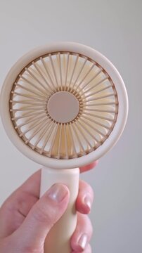 Young woman holding a mini cooling gadget feeling fresh and comfortable outdoors on a warm sunny day.