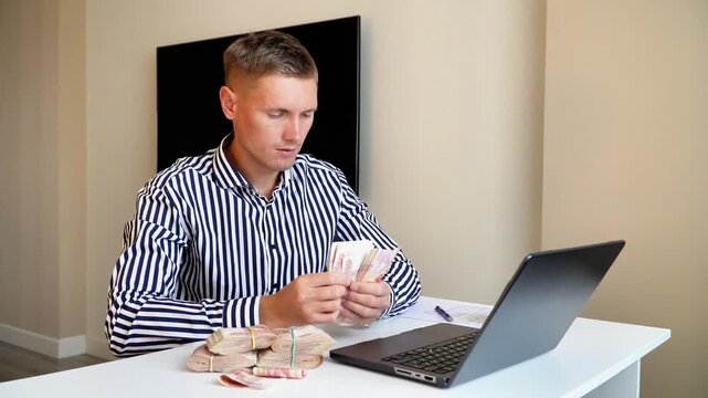 Serious young businessman in a striped white shirt counts a 5,000 thousandth bills checking it on fake. Man counts red paper 5000 rubles bills. A banker checking it on fake a money. A wad of money. 