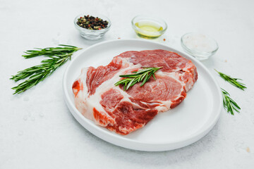 Uncooked pork steak on white plate with rosemary and pepper
