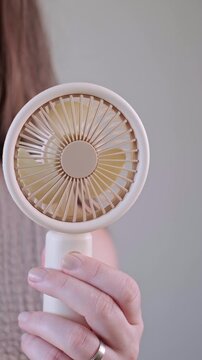 Young woman enjoying cool air from her personal mini fan on a warm sunny day outdoors.