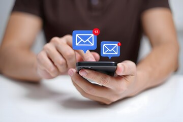 Person holding a smartphone with email notification icons above the device on a white surface