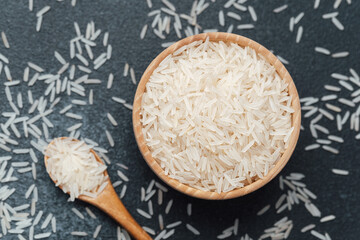 White rice in wooden bowl with scattered grains and wooden spoon