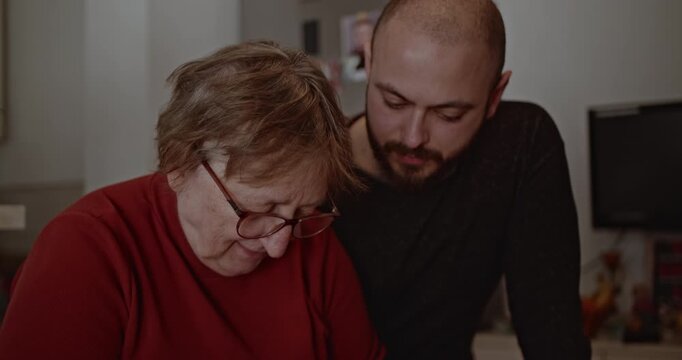A senior woman prepares fresh bread with her son in the kitchen. They share a heartwarming moment of family and tradition.