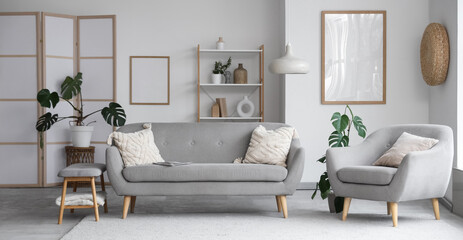 Interior of light living room with grey sofa, armchair and soft bench