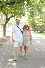 Obraz premium A man and a woman are walking down a street. The man is wearing a white shirt and shorts, and the woman is wearing a dress. They are both carrying handbags. The scene is casual and relaxed