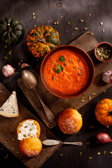 Autumn pumpkin soup with pumpkin seeds, bakery buns, blue cheese, seasonal gourds, shallots, sunflower seeds on rustic wooden boards, healthy homemade comfort food, cozy festive lunch in warm daylight