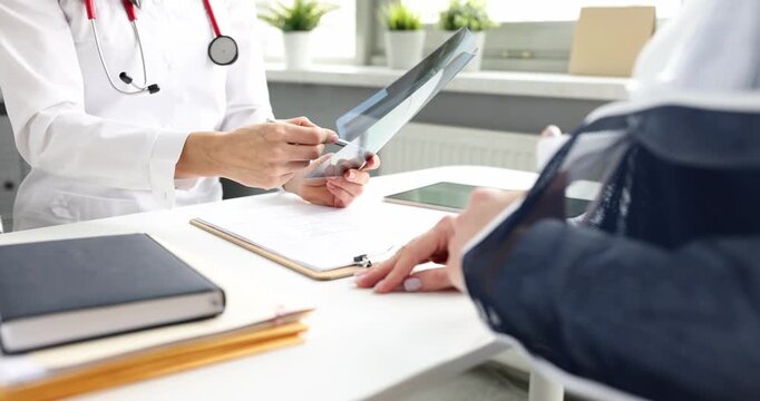 Woman traumatologist examines X-ray image of broken bones consulting patient in hospital. Doctor checks recovery process of lady with arm cast